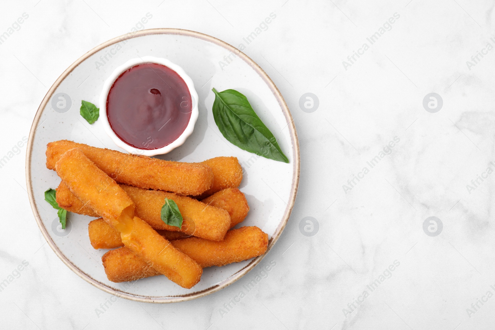 Photo of Tasty fried mozzarella sticks served with tomato sauce and basil on white marble table, top view. Space for text