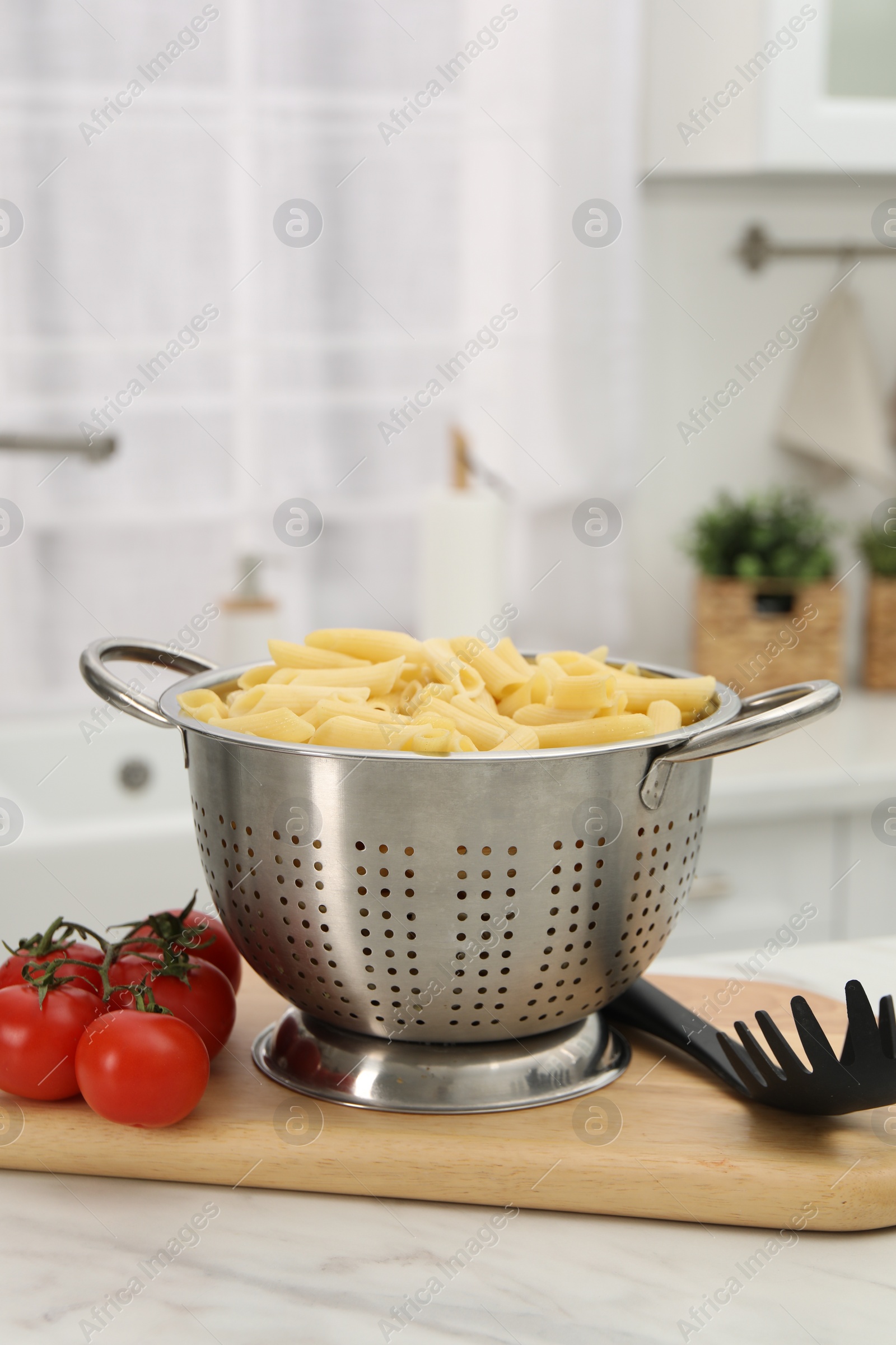 Photo of Cooked pasta in metal colander and tomatoes on light marble table in kitchen