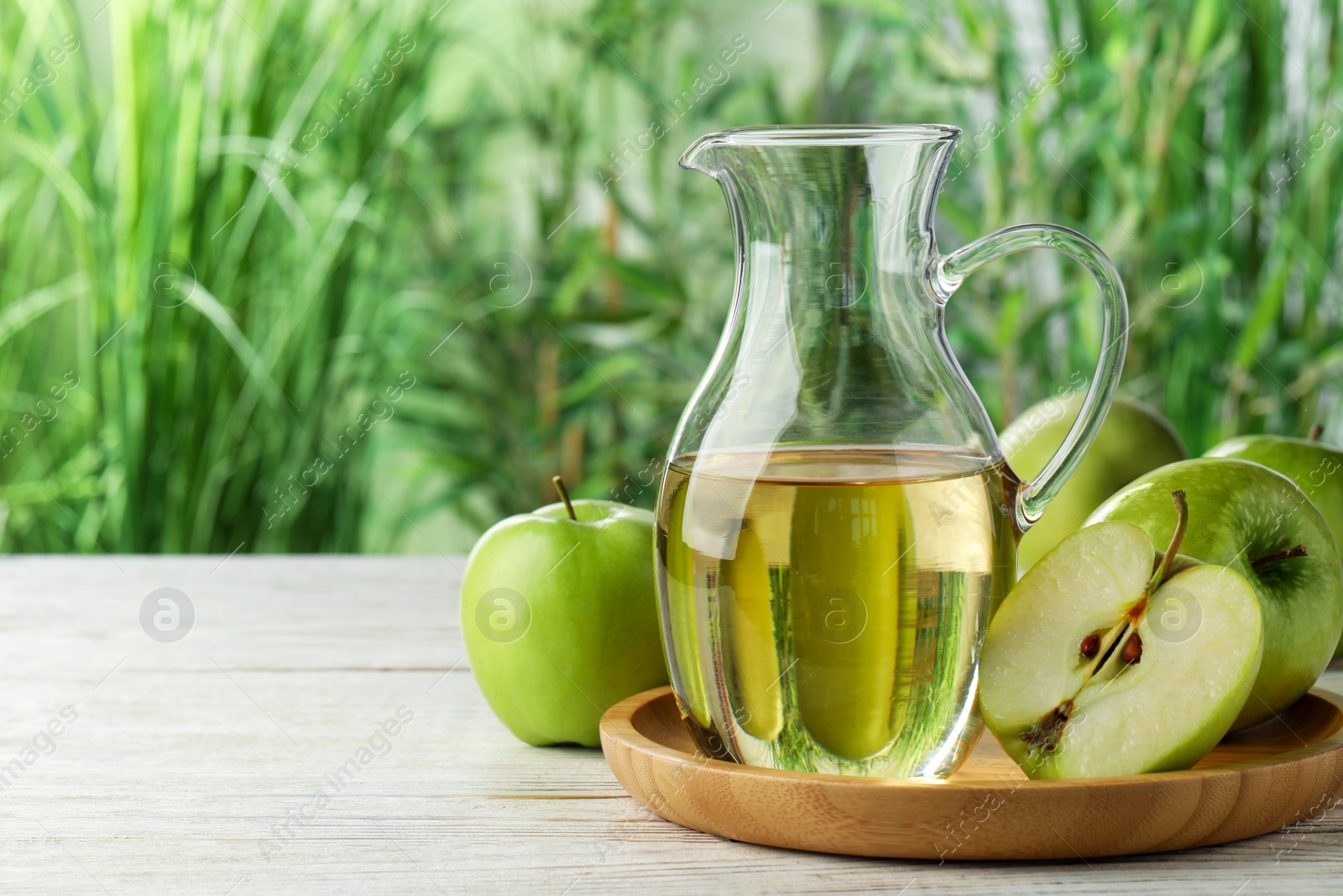 Photo of Jug of tasty juice and fresh ripe green apples on white wooden table outdoors, space for text