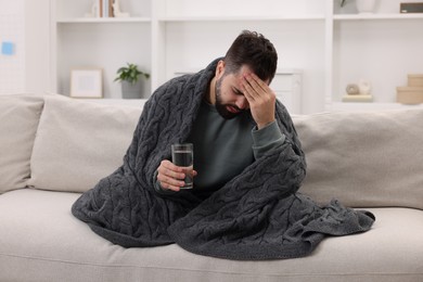 Photo of Man with glass of water suffering from headache on sofa at home