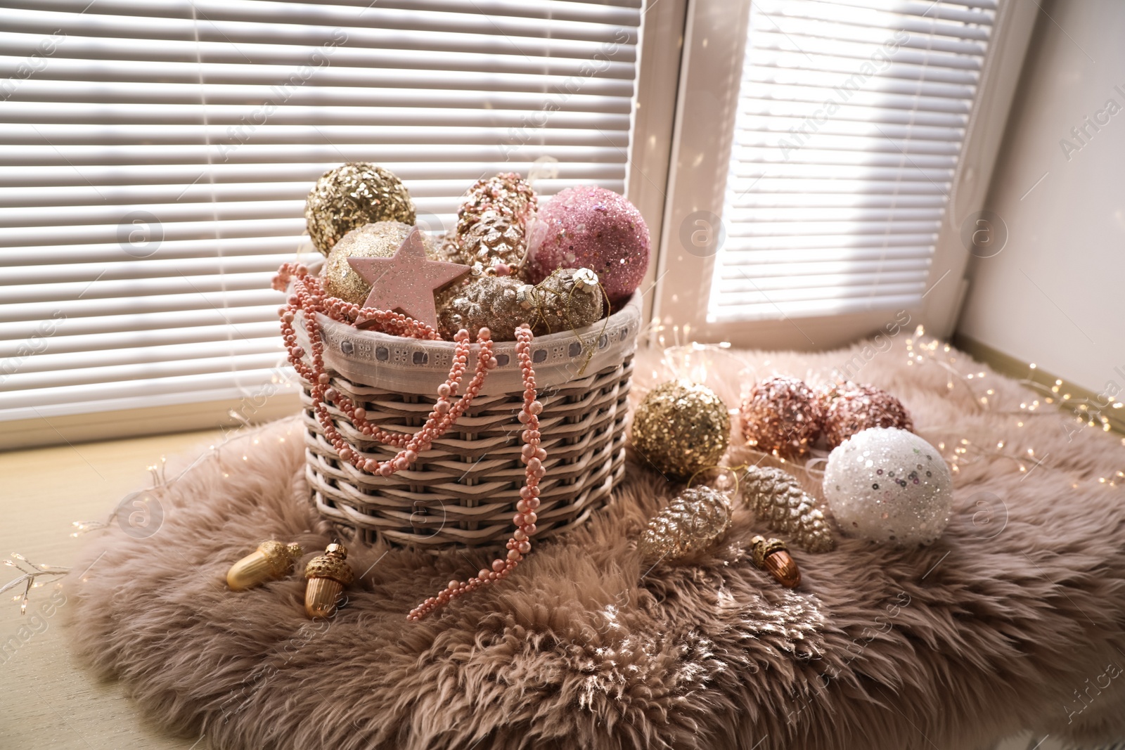 Photo of Basket with beautiful Christmas tree baubles and fairy lights on window sill indoors