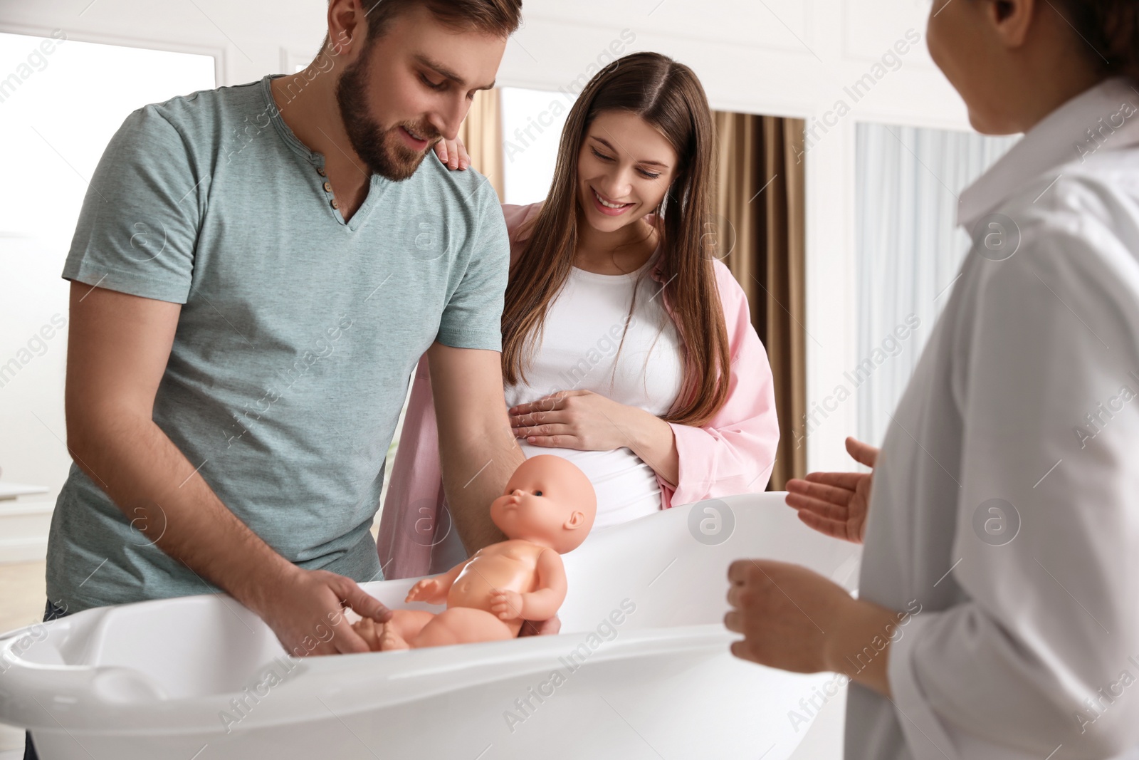 Photo of Man with pregnant wife learning how to bathe baby at courses for expectant parents indoors