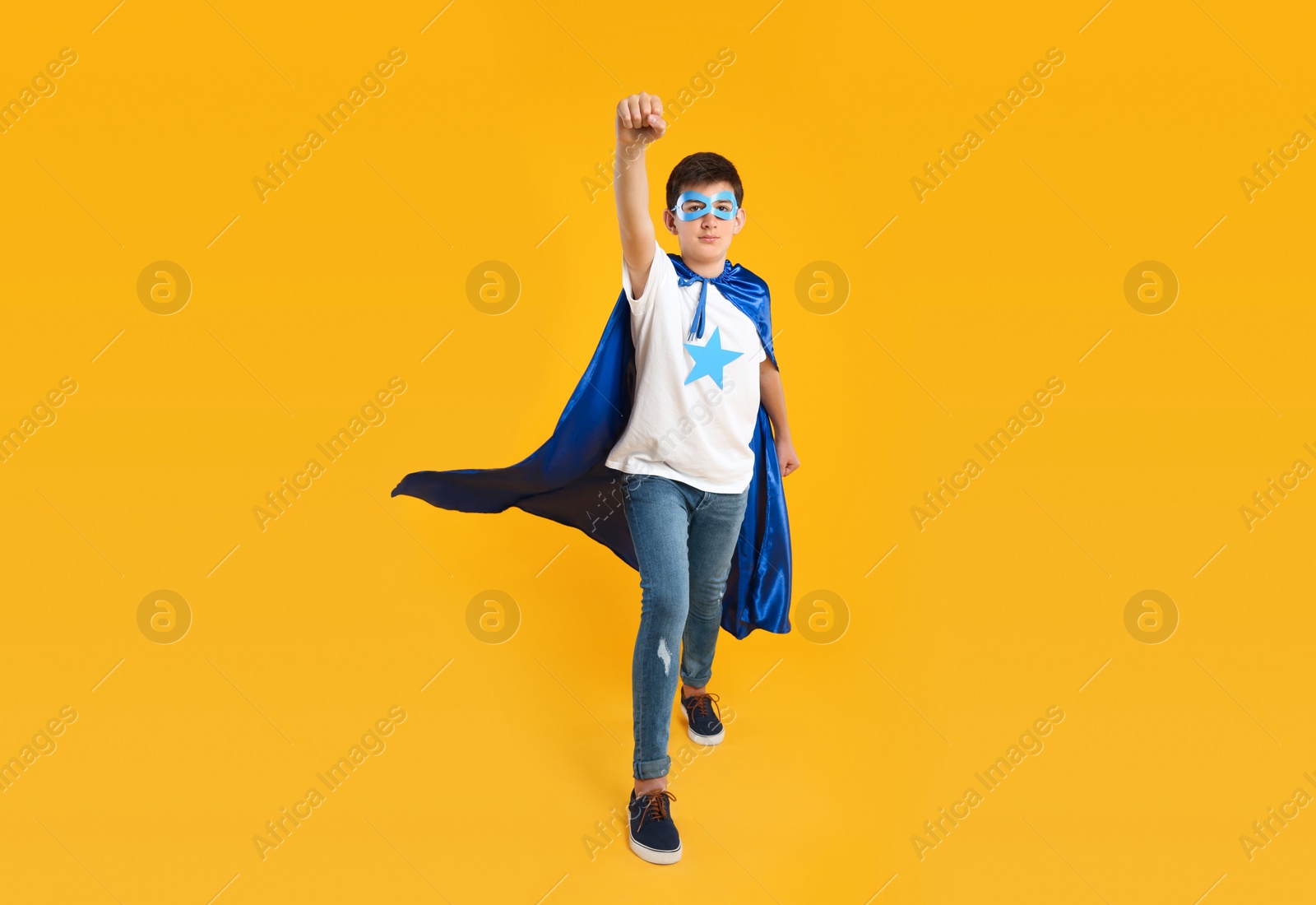 Photo of Teenage boy in superhero costume on yellow background