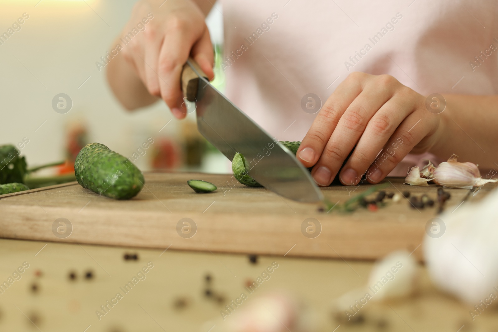 Photo of Woman cutting cucumber at table in kitchen, closeup