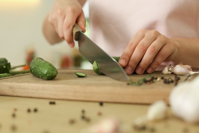 Woman cutting cucumber at table in kitchen, closeup