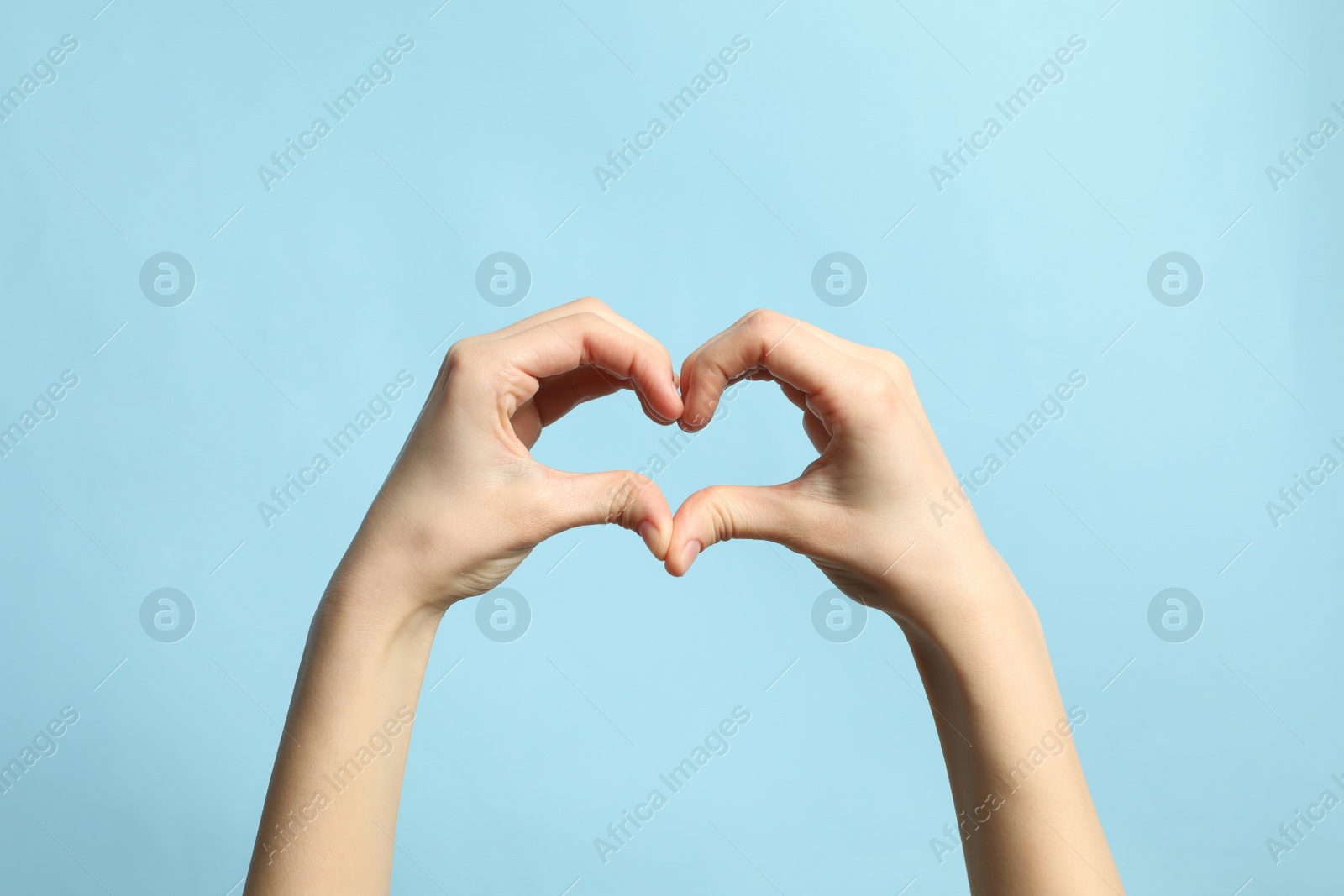 Photo of Woman making heart with her hands on light blue background, closeup