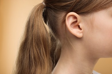 Photo of Hearing problem. Little girl on pale brown background, closeup of ear
