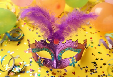 Photo of Beautiful purple carnival mask and party decor on yellow background
