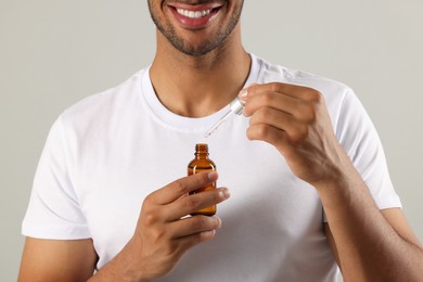 Photo of Man with cosmetic serum in hands on light grey background, closeup