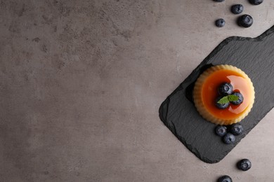 Photo of Delicious caramel pudding with blueberries and mint on grey table, flat lay. Space for text