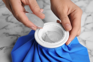 Photo of Woman putting ice cubes into pack at marble table, closeup