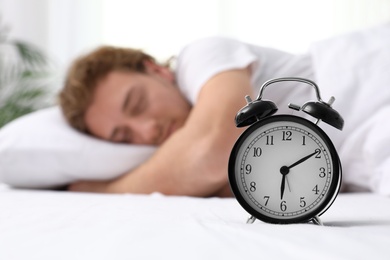 Photo of Alarm clock and blurred sleepy man on background, space for text. Bedtime