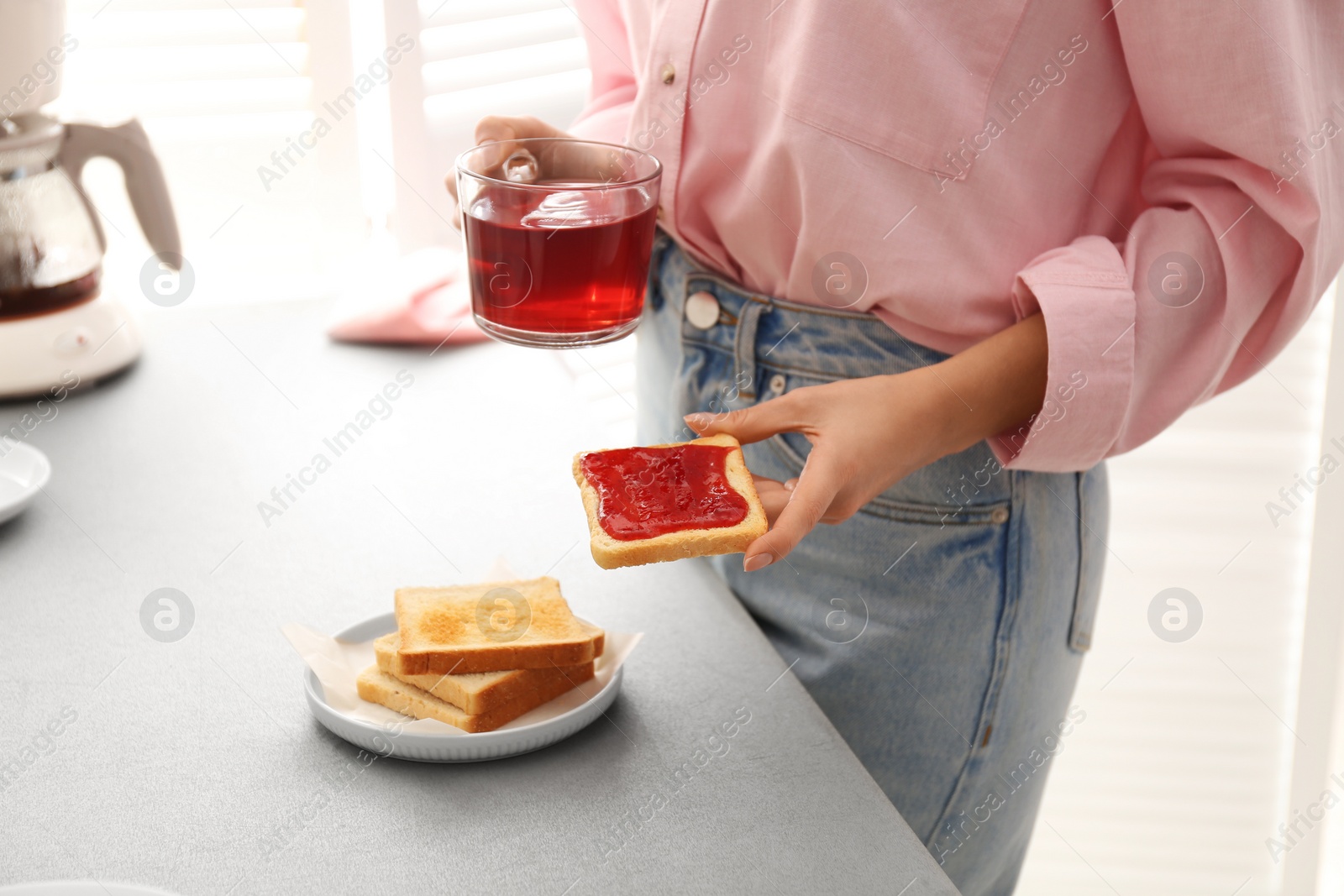 Photo of Woman having tasty breakfast with toast and raspberry tea at home, closeup. Morning routine