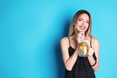 Photo of Young woman with mason jar of tasty lemonade on color background. Natural detox drink
