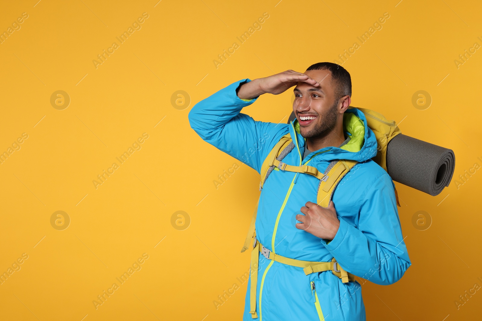 Photo of Happy tourist with backpack on yellow background, space for text