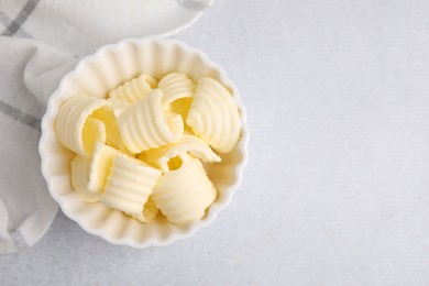 Photo of Tasty butter curls in bowl on light grey table, top view. Space for text