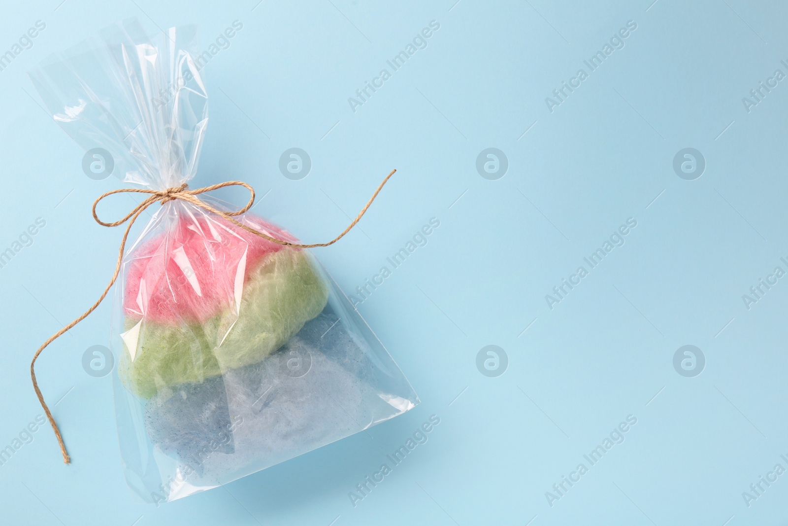 Photo of Packaged sweet cotton candy on light blue background, top view. Space for text