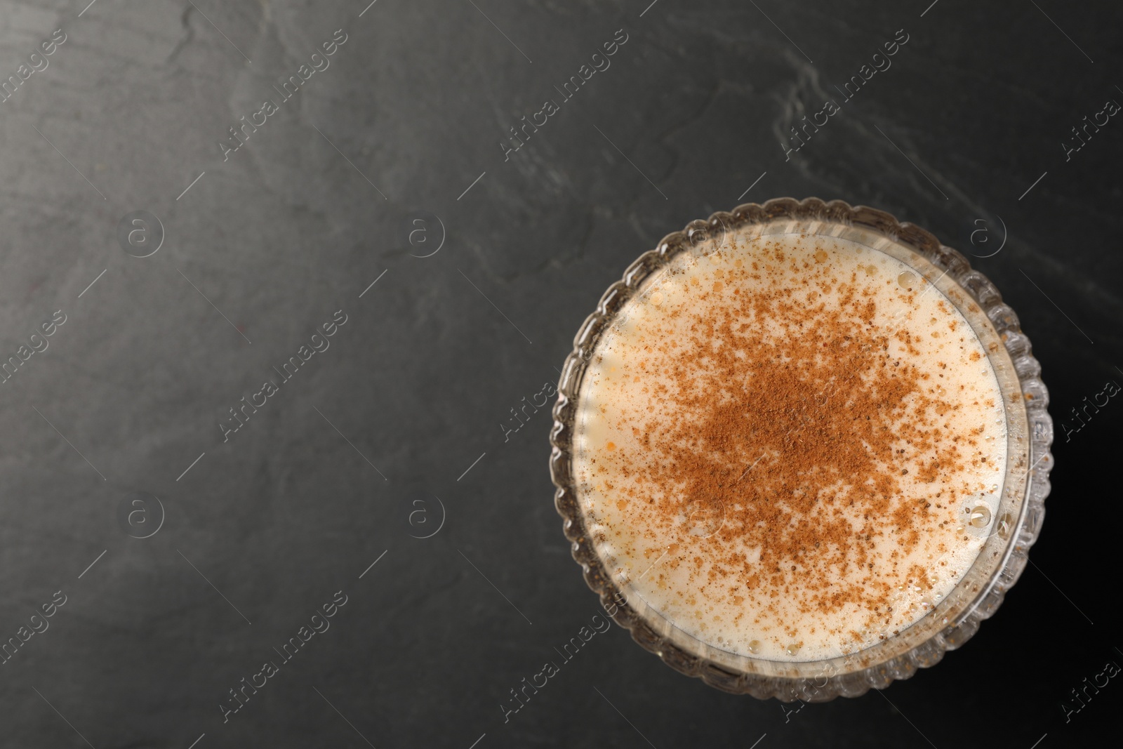 Photo of Glass of delicious eggnog on dark marble table, top view. Space for text