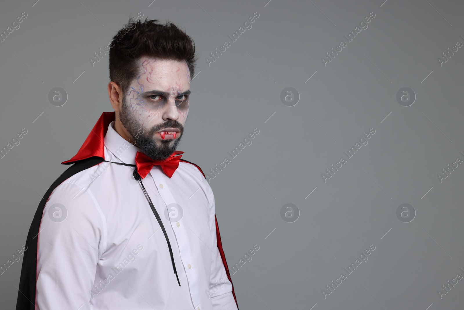 Photo of Man in scary vampire costume with fangs on light grey background, space for text. Halloween celebration