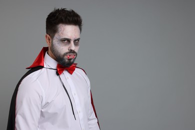 Man in scary vampire costume with fangs on light grey background, space for text. Halloween celebration