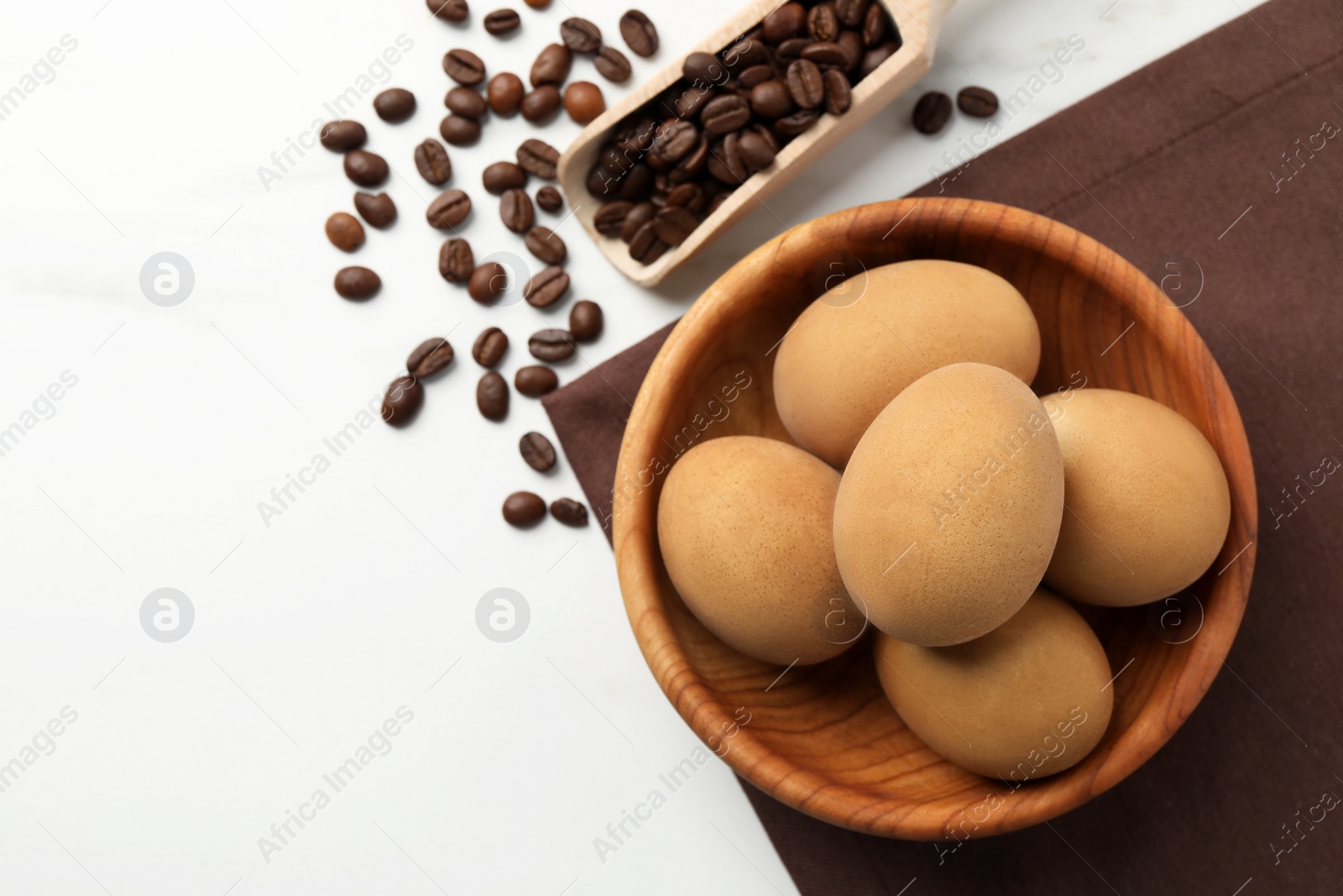 Photo of Easter eggs painted with natural dye in wooden bowl and coffee beans on white table, flat lay. Space for text