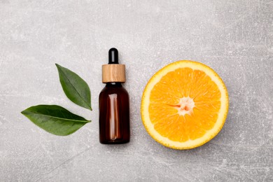 Bottle of essential oil with orange slice and leaves on grey table, flat lay