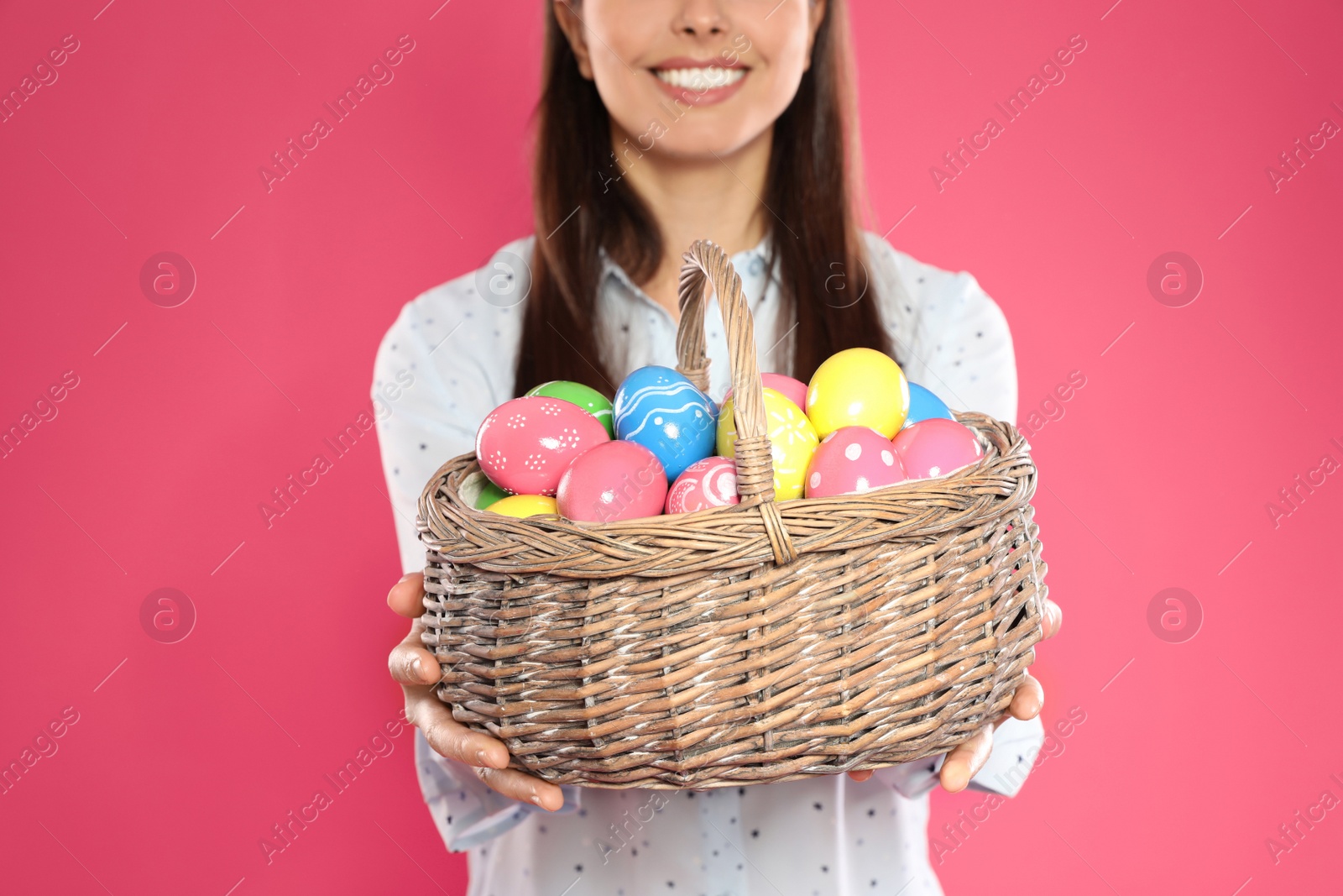 Photo of Beautiful woman holding basket with Easter eggs on color background, closeup