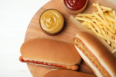 Photo of Composition with hot dogs, french fries and sauce on wooden board, top view