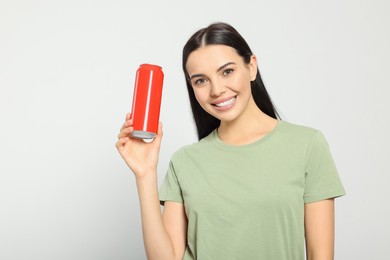 Beautiful happy woman holding red beverage can on light grey background