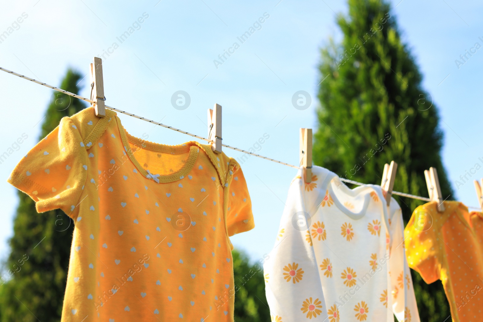 Photo of Clean baby onesies hanging on washing line in garden. Drying clothes