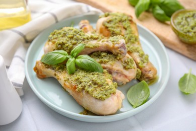 Delicious fried chicken drumsticks with pesto sauce and basil on white table, closeup