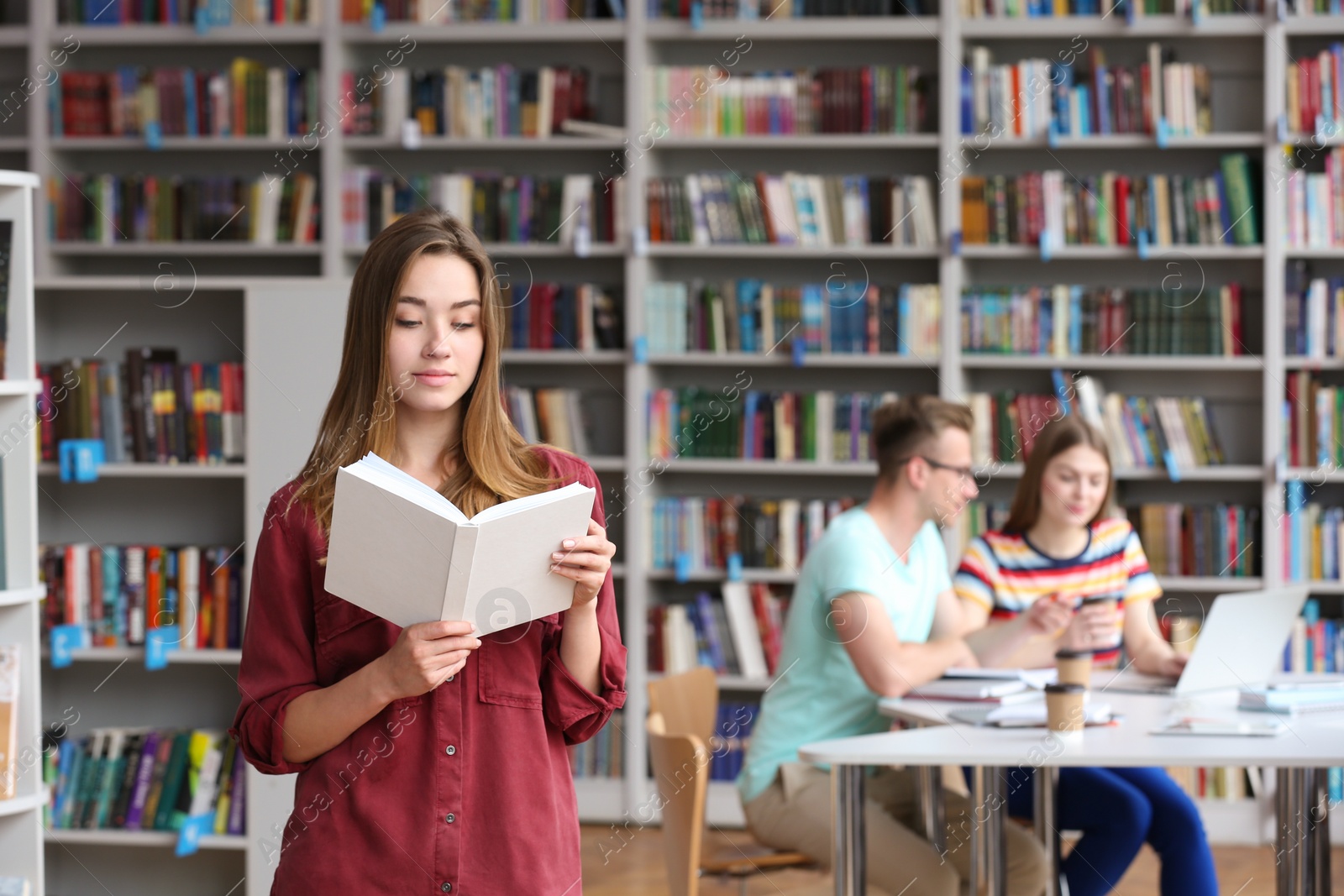 Photo of Young pretty woman reading book in library. Space for text