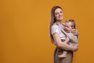 Mother holding her child in sling (baby carrier) on orange background. Space for text