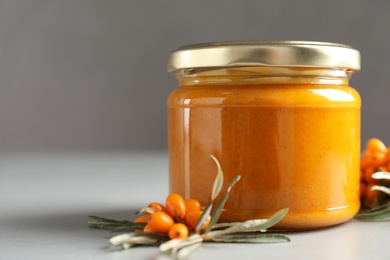 Delicious sea buckthorn jam and fresh berries on grey table, closeup. Space for text