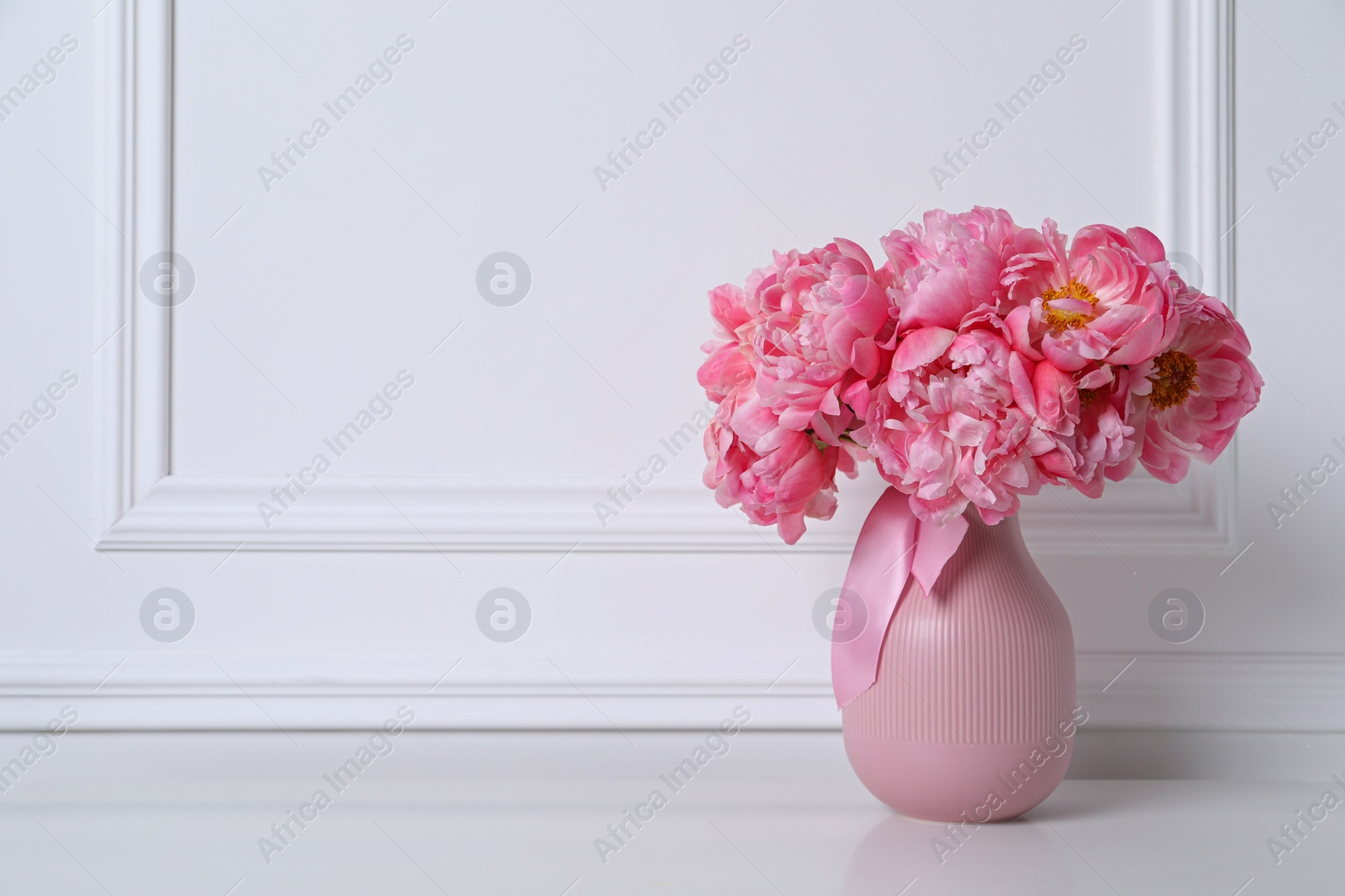 Photo of Beautiful bouquet of pink peonies in vase near white wall. Space for text