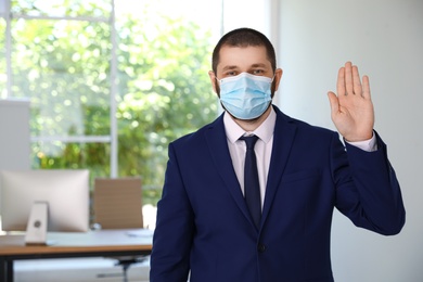Man in protective face mask showing hello gesture in office. Keeping social distance during coronavirus pandemic