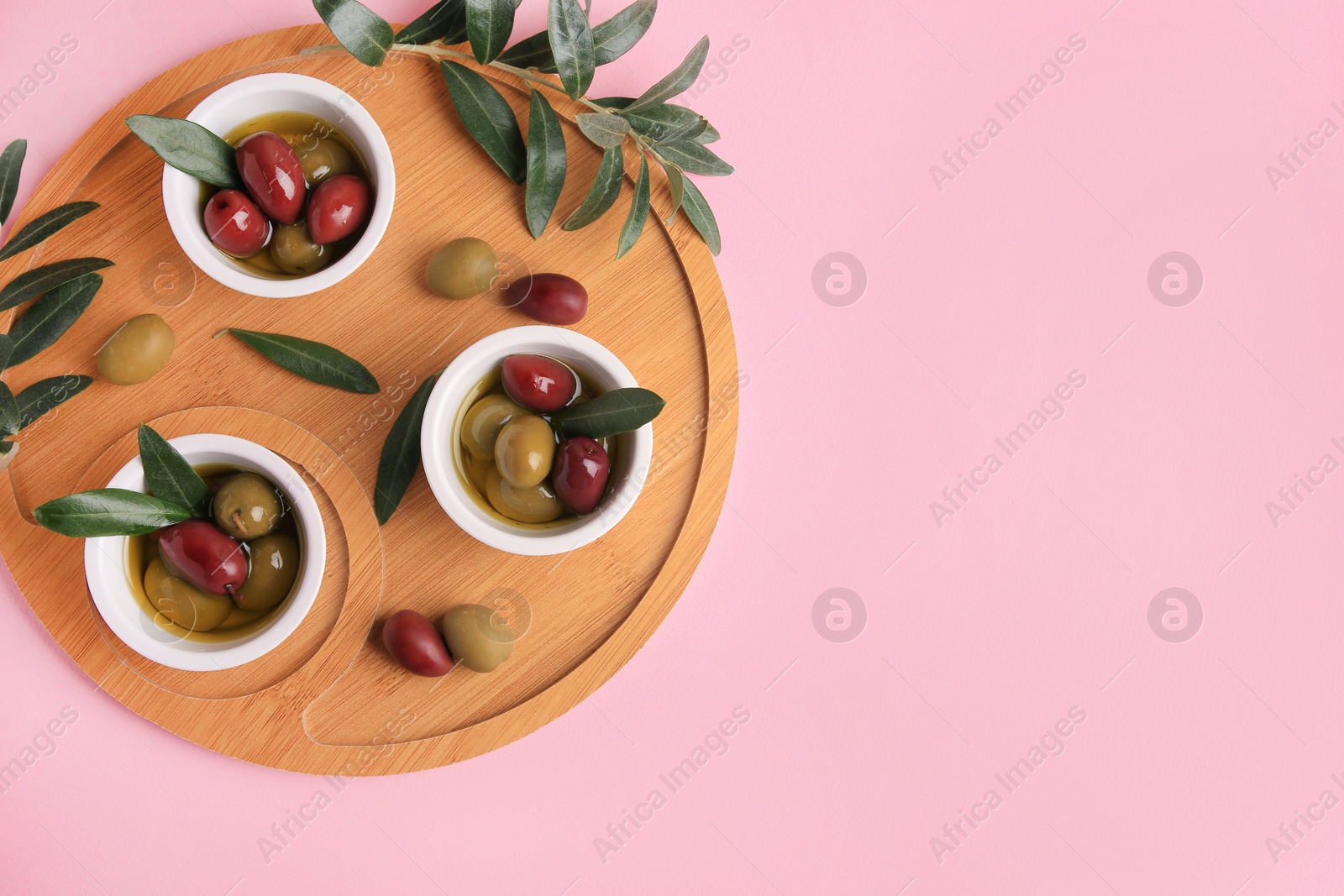 Photo of Wooden tray with different ripe olives and leaves on pink background, flat lay. Space for text