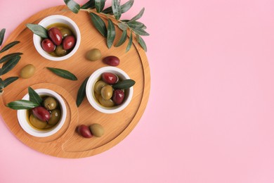 Wooden tray with different ripe olives and leaves on pink background, flat lay. Space for text