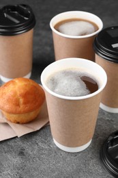 Photo of Coffee to go. Paper cups with tasty drink and muffin on grey table, closeup