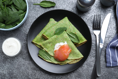 Delicious spinach crepes with salmon and cream served on grey table, flat lay