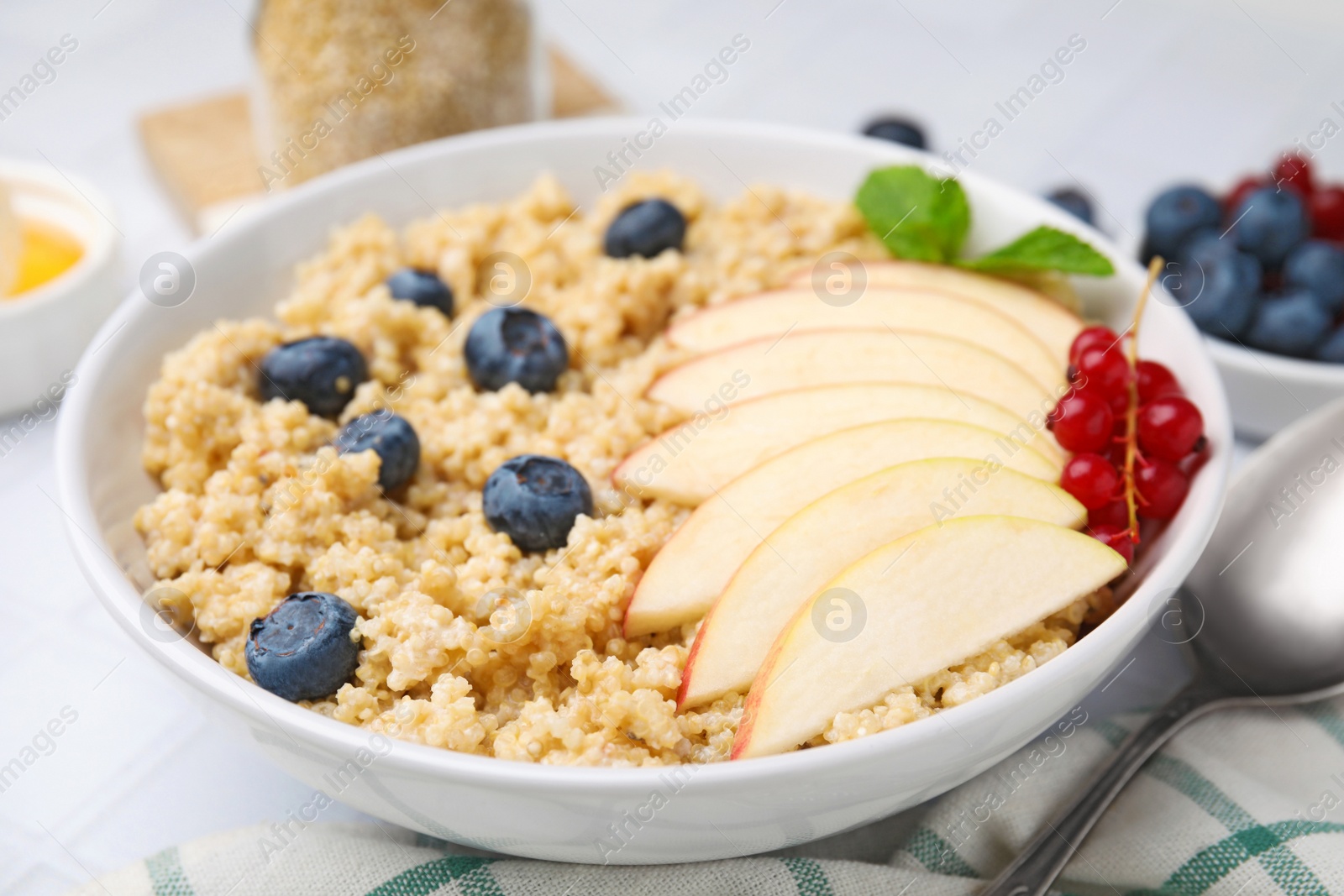 Photo of Bowl of delicious cooked quinoa with apples, blueberries and cranberries on white tiled table, closeup