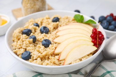 Bowl of delicious cooked quinoa with apples, blueberries and cranberries on white tiled table, closeup