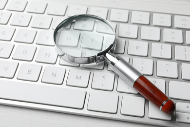 Photo of Magnifier glass and keyboard on white table, closeup. Find keywords concept