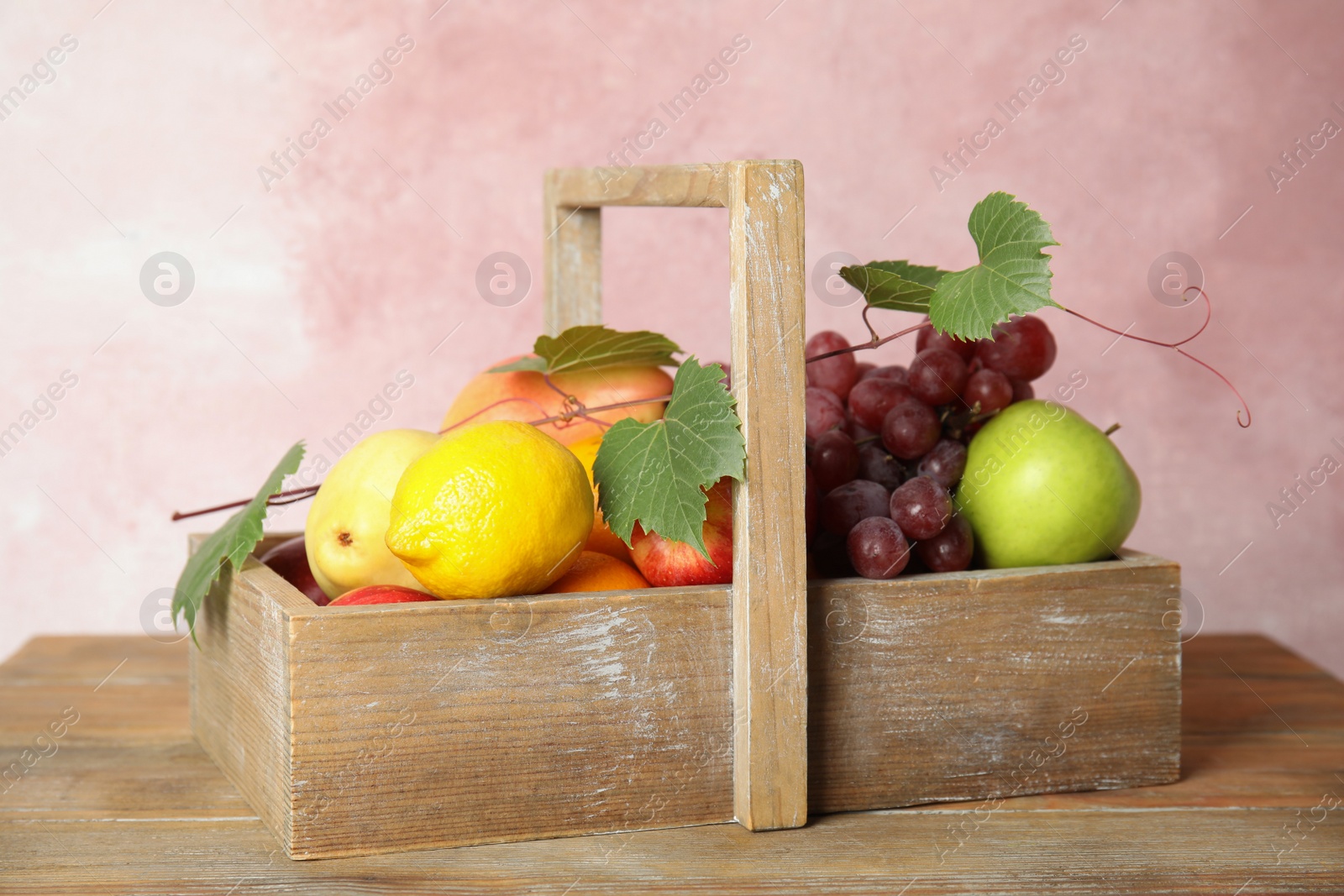 Photo of Crate with different fruits on wooden table near pink wall