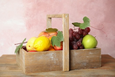 Photo of Crate with different fruits on wooden table near pink wall