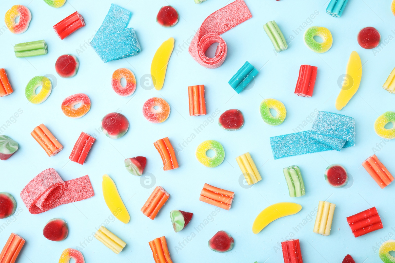 Photo of Many different jelly candies on light blue background, flat lay