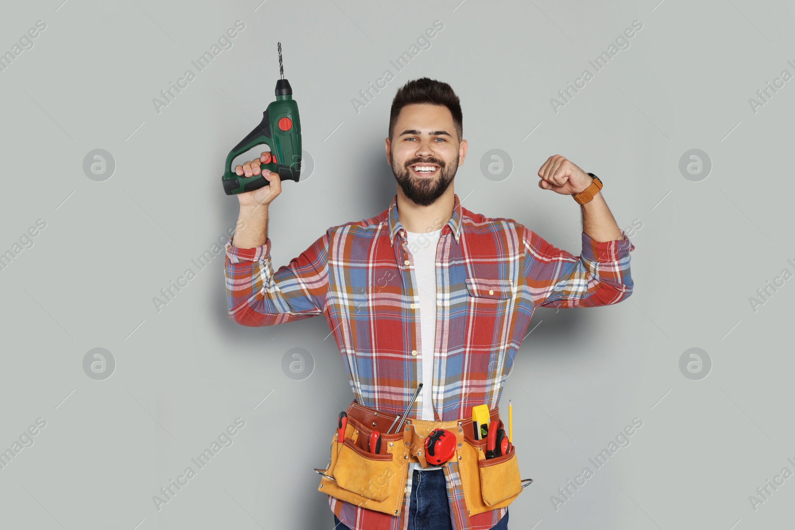 Photo of Young worker with power drill and tool belt on grey background