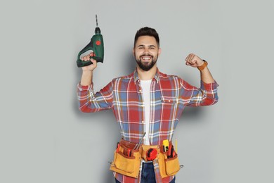 Photo of Young worker with power drill and tool belt on grey background