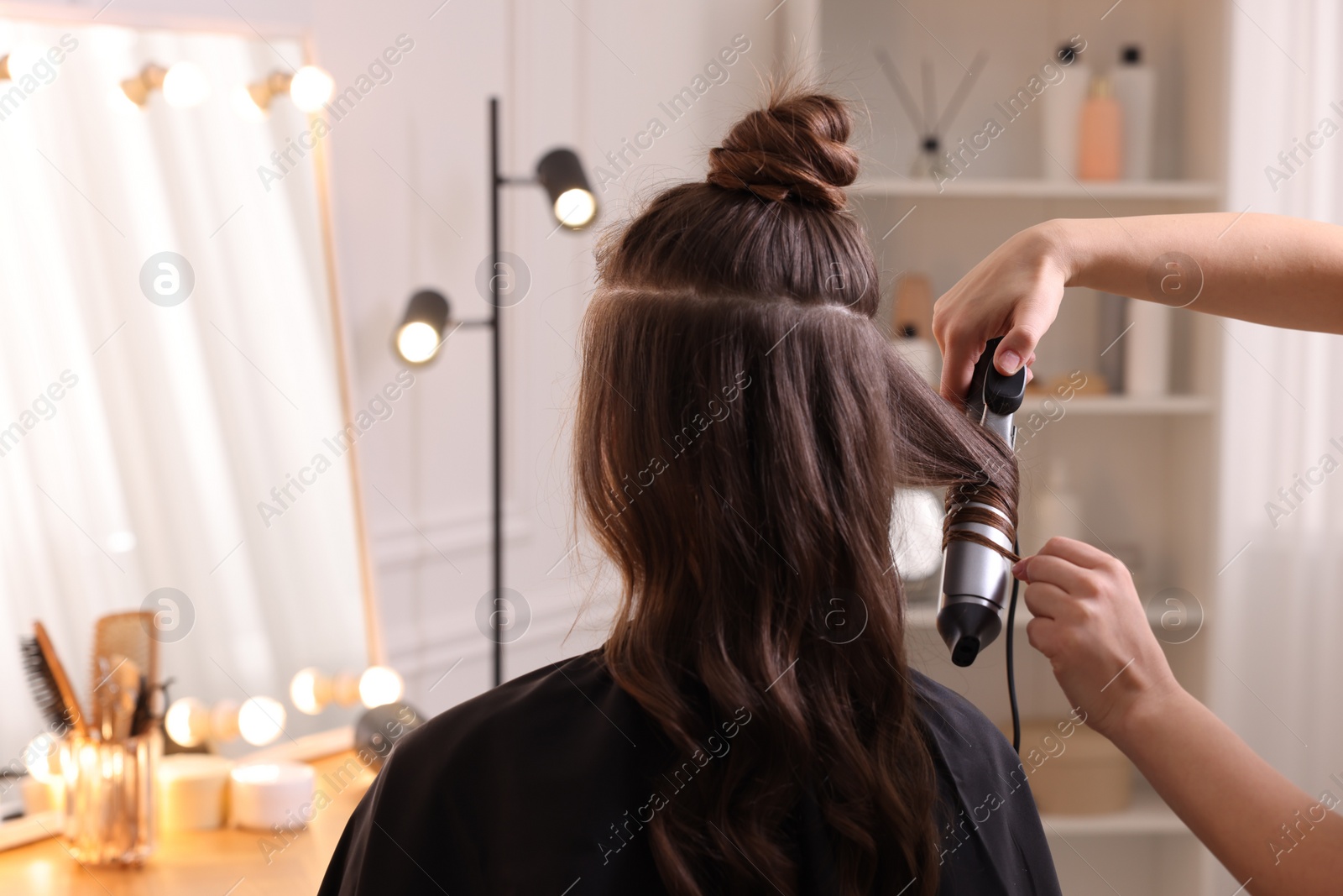 Photo of Hairdresser using curling hair iron while working with woman in salon, closeup