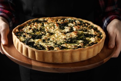 Woman holding delicious homemade spinach quiche on dark background, closeup